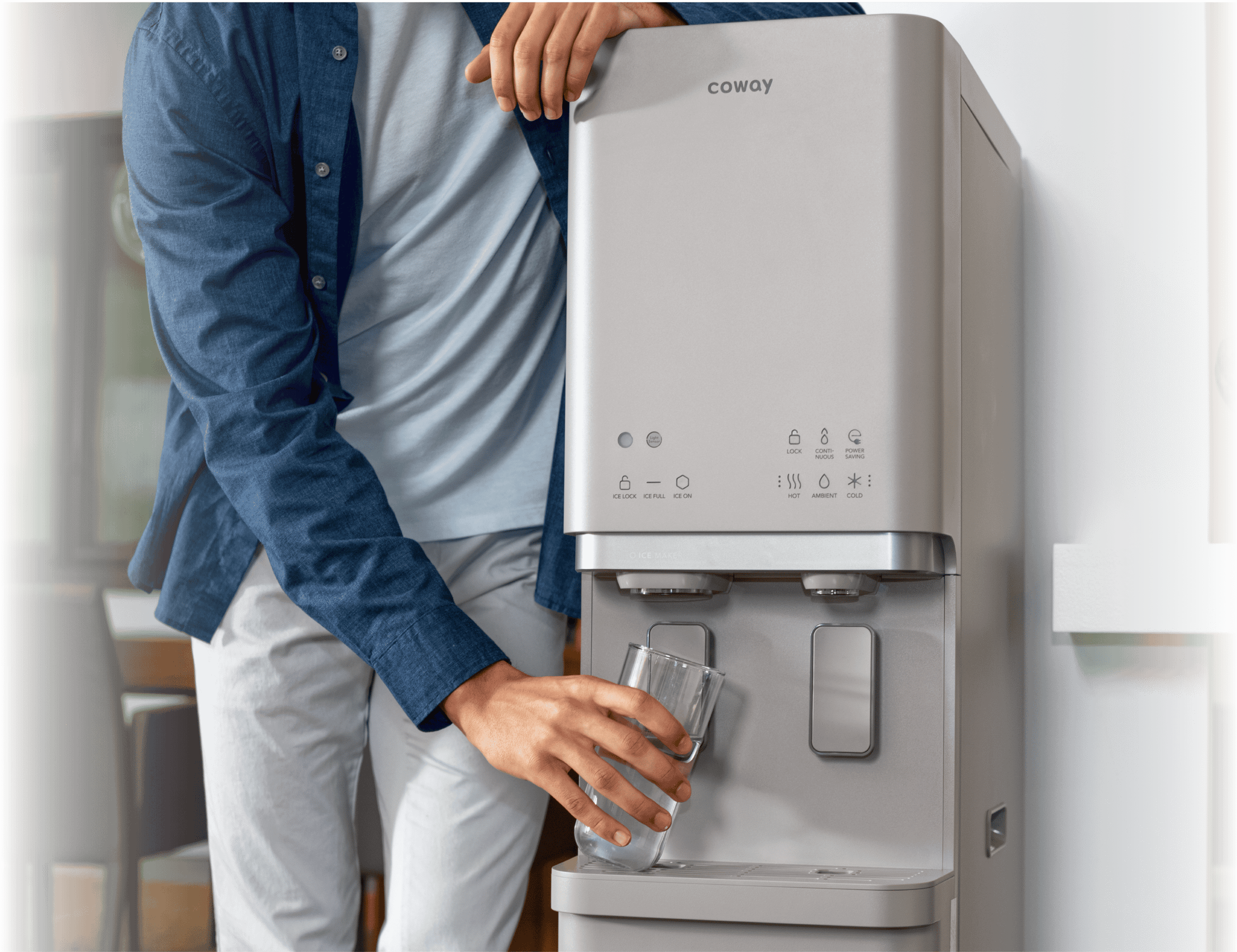 Person filling a glass with water from a Coway water purifier inside a room.