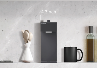 Compact Coway P-2211N water purifier measuring 4.3 inches wide on a kitchen counter with wooden spoons in a white vase, a black mug, and a bottle of oil.