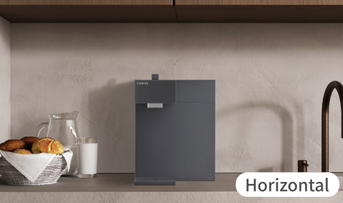 Modern black Coway P-2211N water purifier on a kitchen counter with a basket of bread, glass, and carafe of milk beside it.