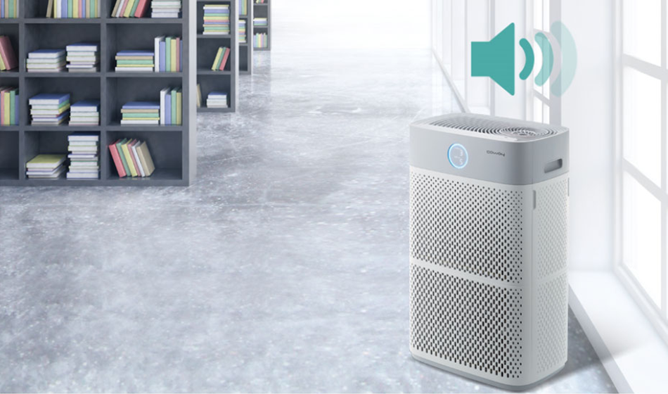 Coway AP-3018B air purifier with sound icon indicating operational noise, placed on a floor near large windows in a room with bookshelves.