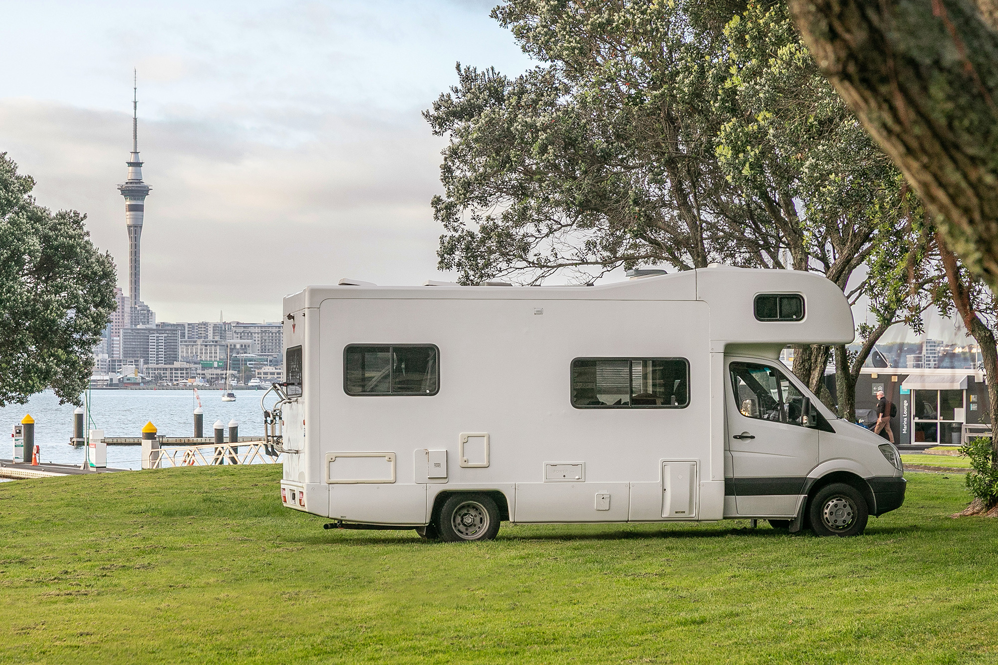 A motorhome parked on the grass at Bayswater Marina, with the Sky Tower across the harbour