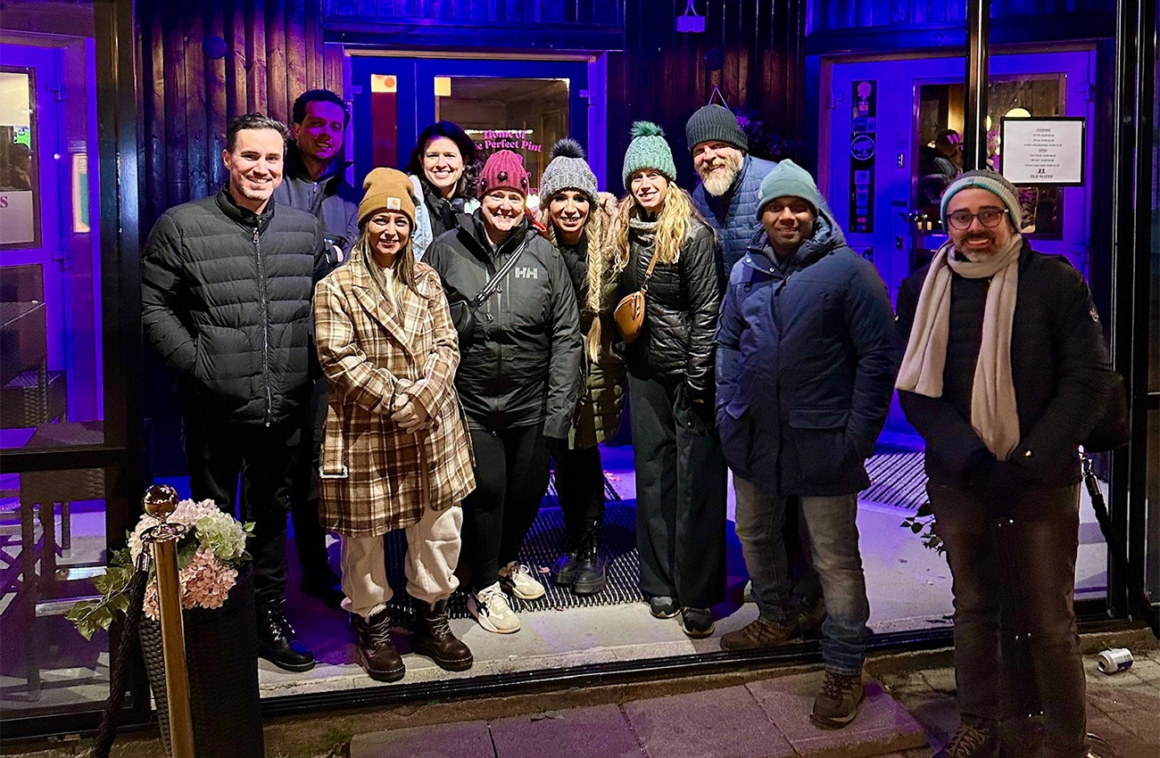 Group of ten people wearing winter clothes and hats standing outside a building with blue lighting at night.
