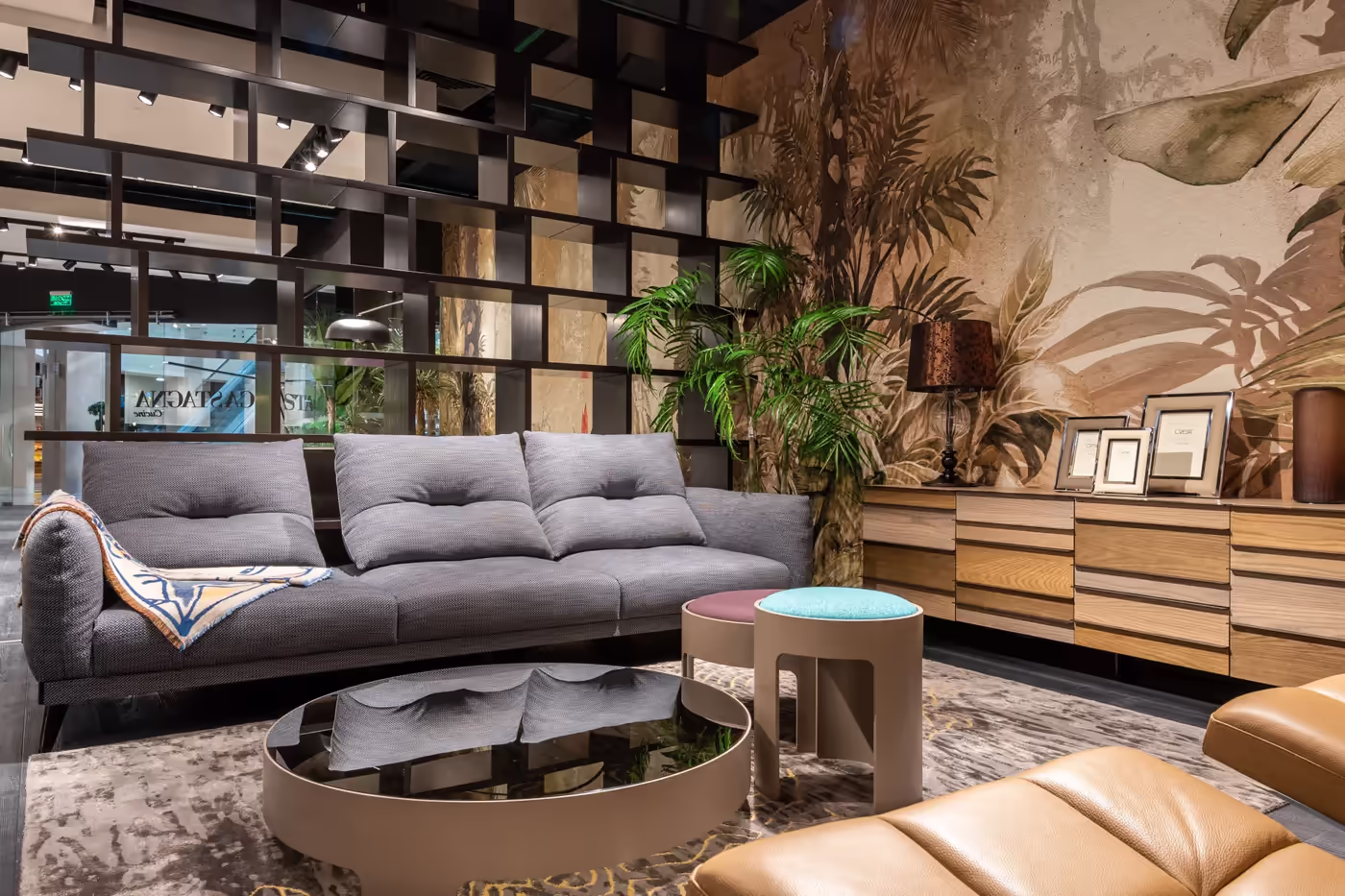 Le showroom d’un magasin de meubles : canapé gris, tables basses rondes, buffet en bois et plantes.