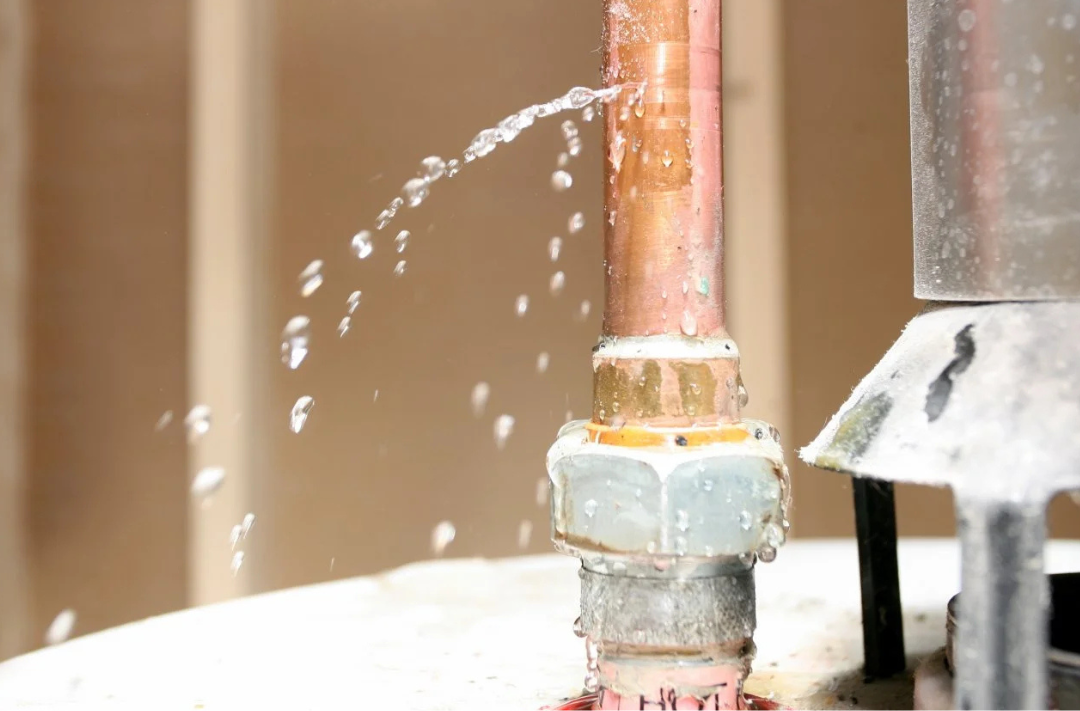 Close-up of leaking copper pipe with water spraying, illustrating pipe burst restoration and repair in Calgary
