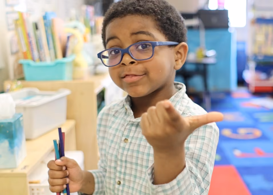Smiling student pointing with his thumb in a classroom