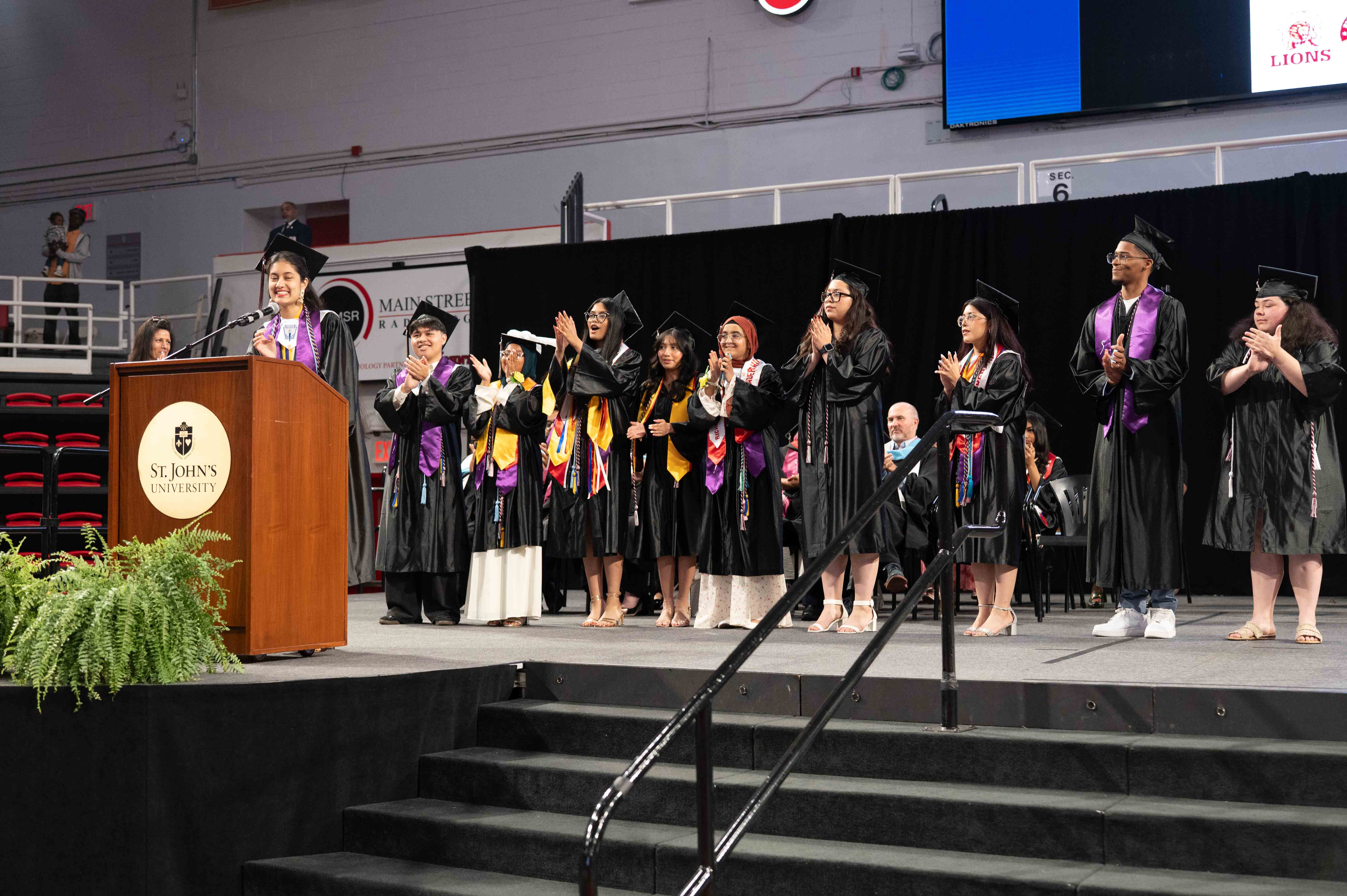 Graduates in caps and gowns applauding on stage at commencement ceremony