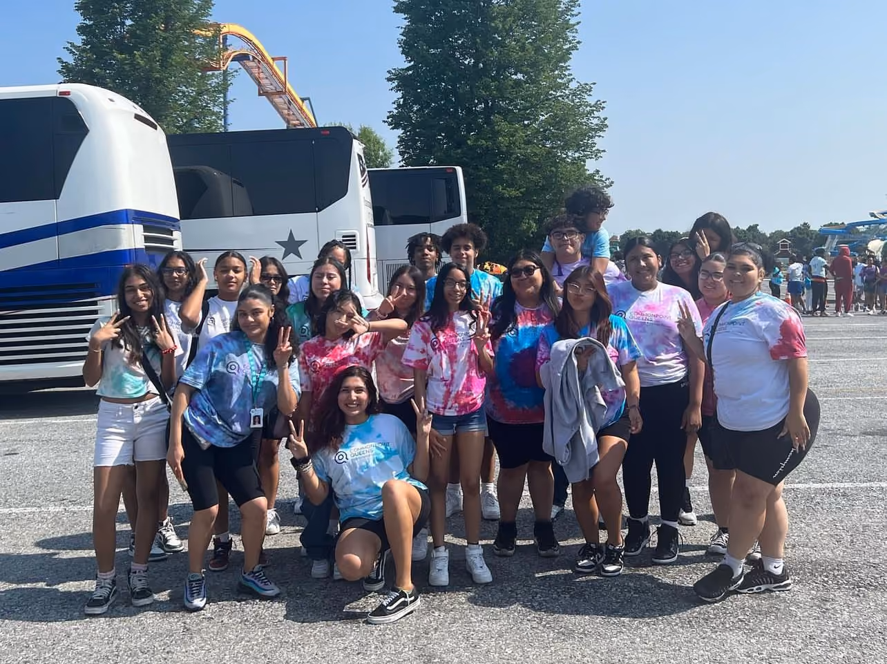 Students in matching tie-dye shirts posing together at amusement park field trip