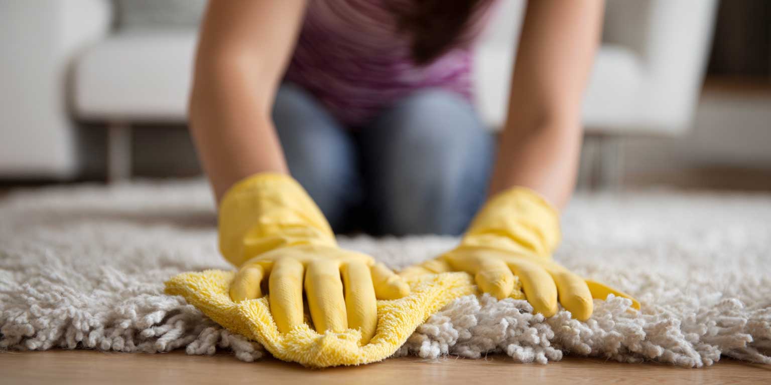 Yellow push broom sweeping a shiny wet tiled floor in a spacious room with large windows.