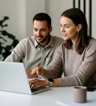 Man and woman collaborating and pointing at laptop screen at a table.