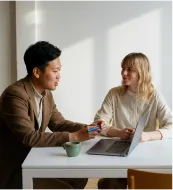 Man and woman having a friendly discussion at a table with a laptop and coffee mug.
