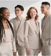 Four diverse young professionals in light beige business suits smiling and standing together.