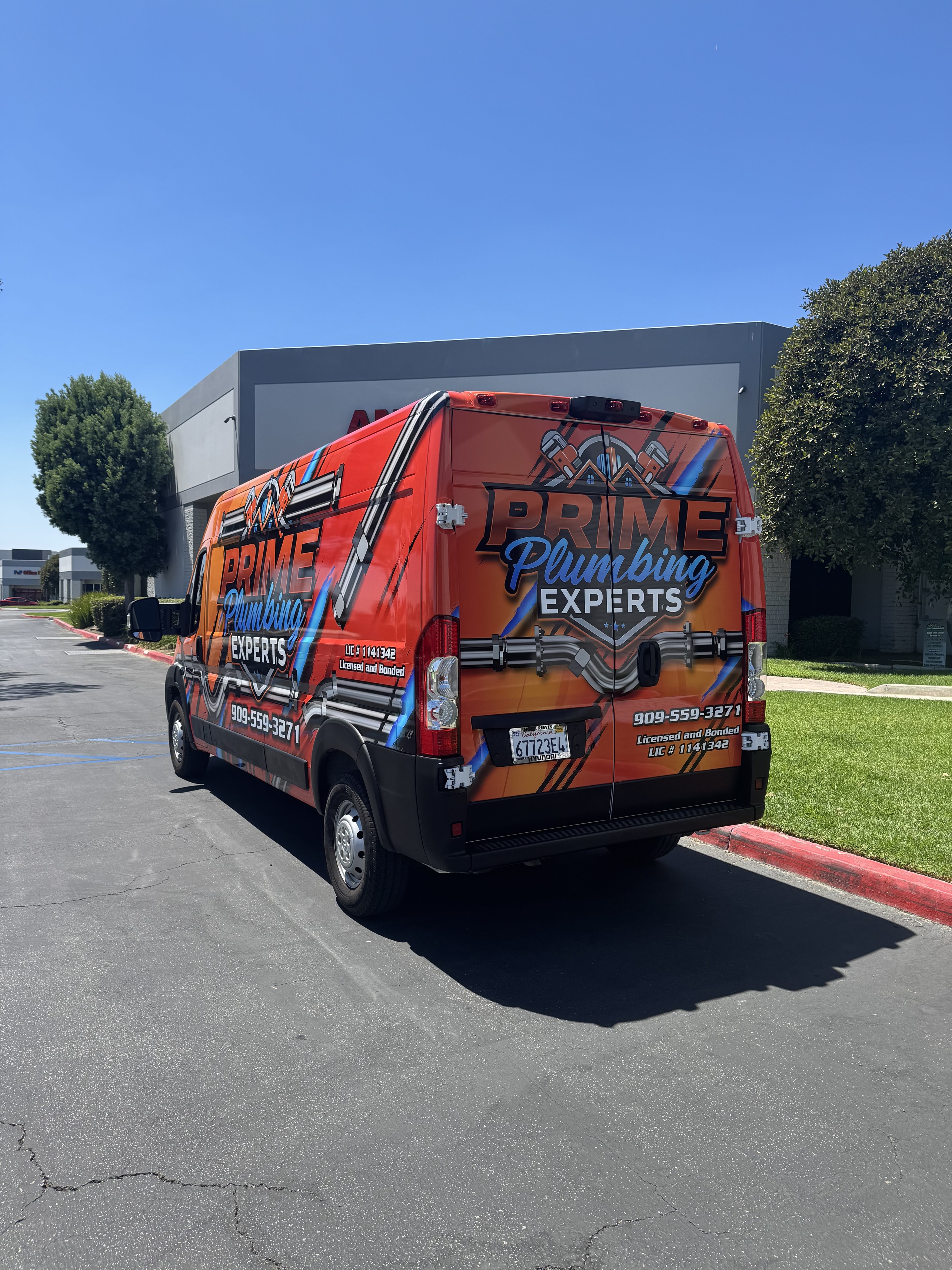 Orange Prime Plumbing Experts work van parked outside a commercial building on a sunny day.