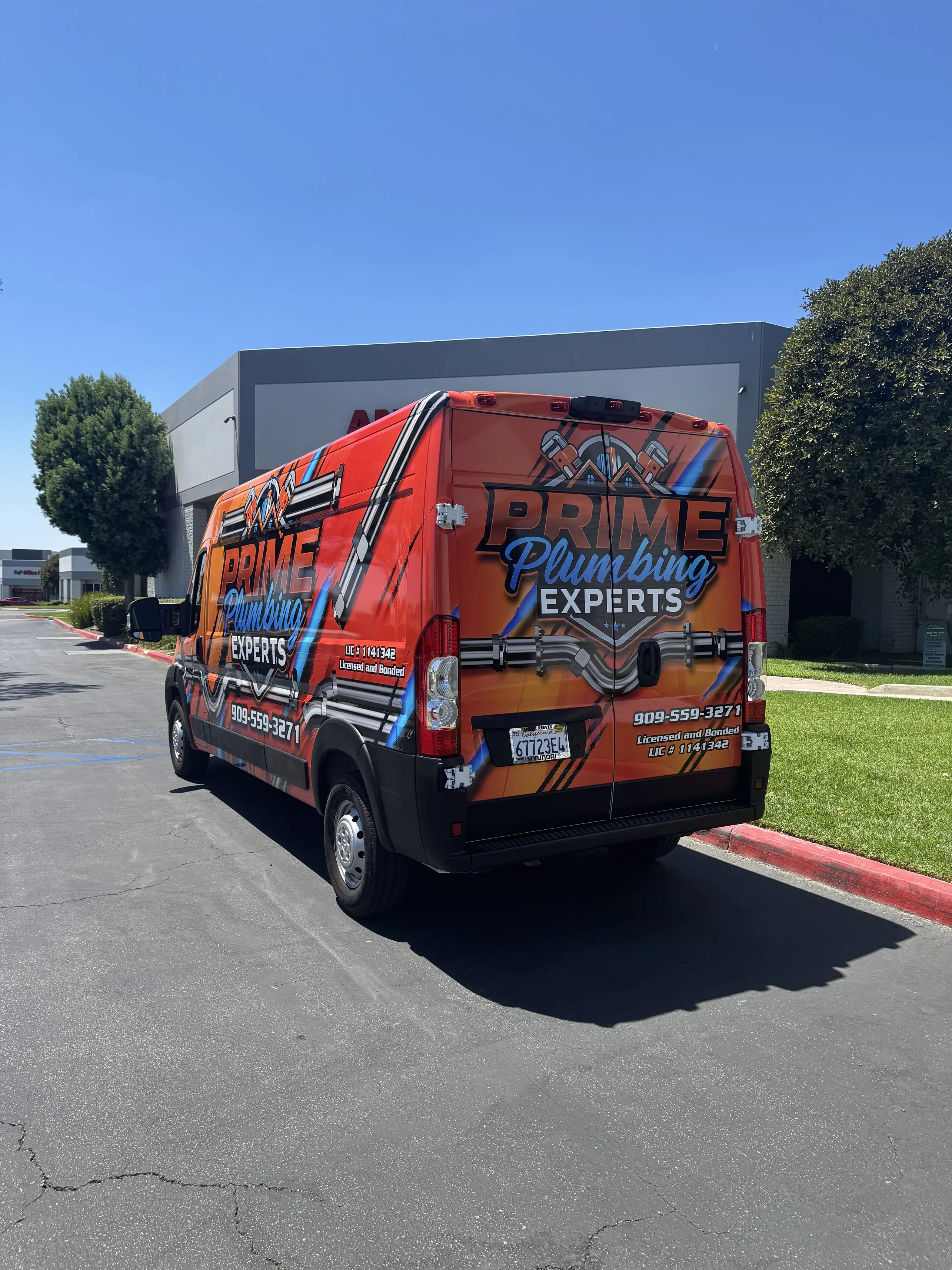 Orange Prime Plumbing Experts work van parked outside a commercial building on a sunny day.