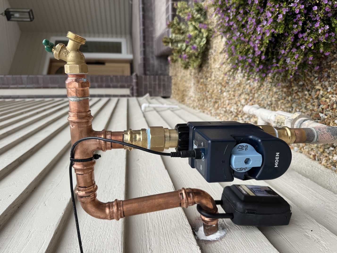 Moen smart water shutoff valve attached to copper outdoor plumbing near a house exterior wall.