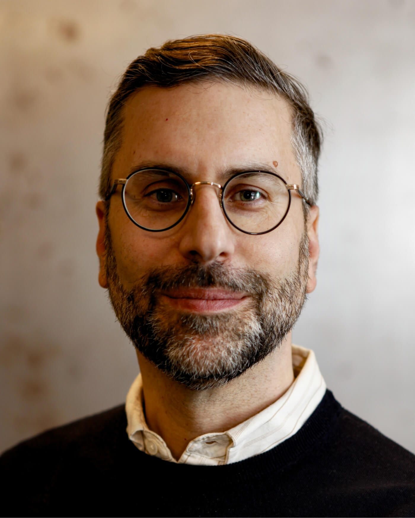 Närbild av man med glasögon, skägg och kort hår som ler mot kameran.