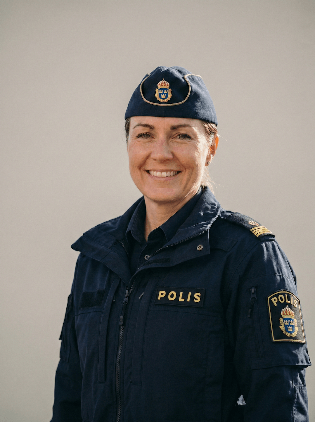 Leende kvinnlig svensk polis i uniform och mössa med polisemblem.