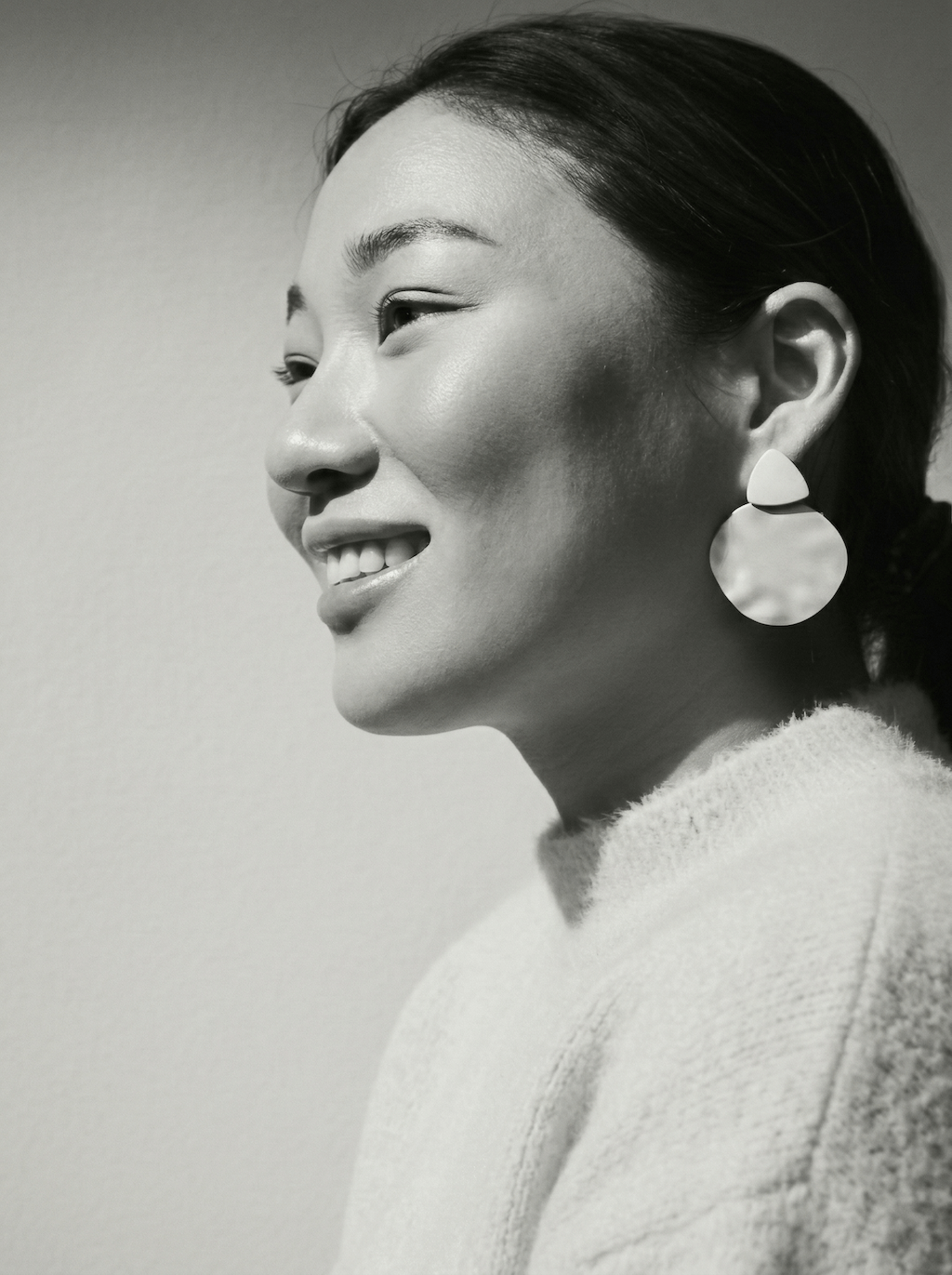 Porträtt av en leende kvinna med stora örhängen och stickad tröja i svartvitt.