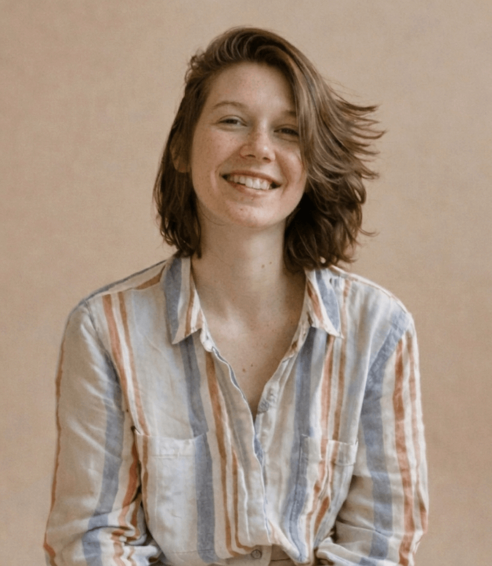 Leende ung kvinna med axellångt brunt hår och randig skjorta i mjuka färger mot beige bakgrund.