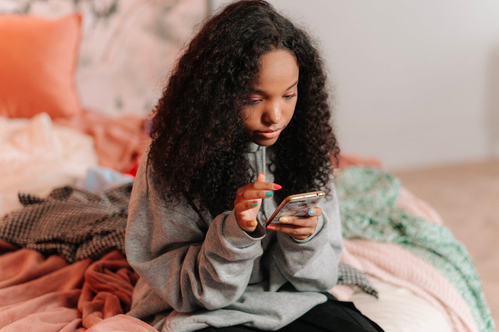 A young woman sitting on her bed using her cellphone
