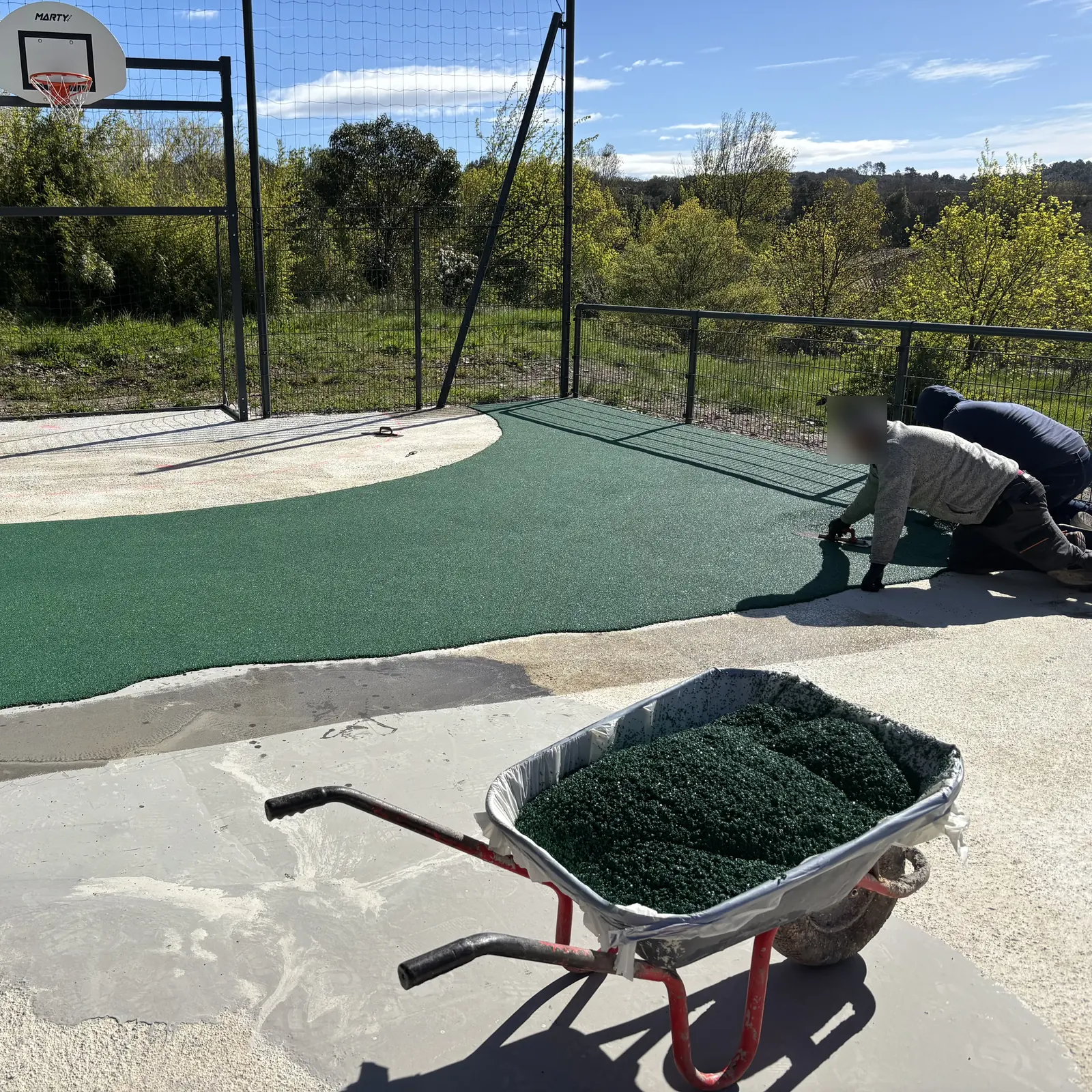 Applicateurs lissant un sol amortissant vert sur un terrain multisport