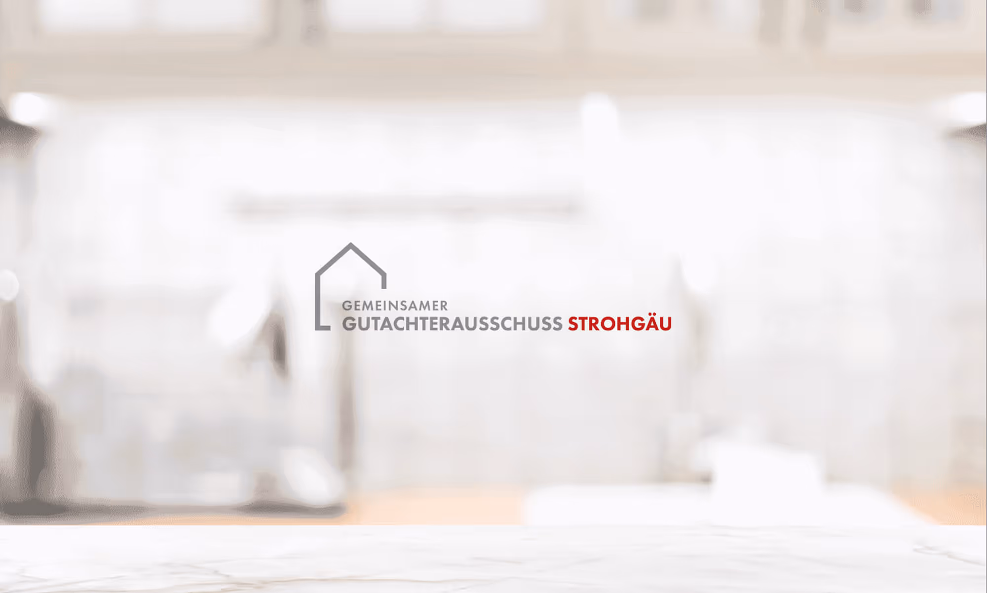 Logo with a house outline and text 'GEMEINSAMER GUTACHTERAUSSCHUSS STROHGÄU' on a blurred kitchen background.