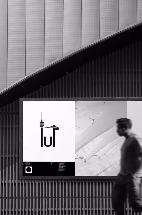 Black and white street billboard with minimalist building and crane graphic on left and blurred man walking past on right.