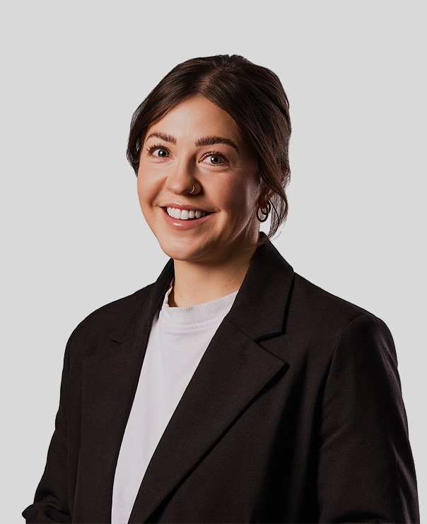Smiling woman with brown hair, hoop earrings, black blazer, and white shirt on light gray background.