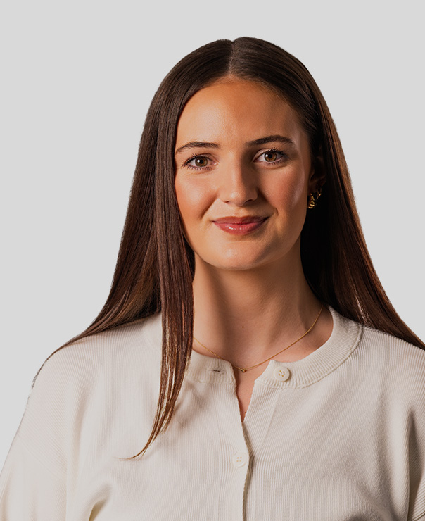 Young woman with long straight brown hair wearing a white buttoned shirt and gold necklace.