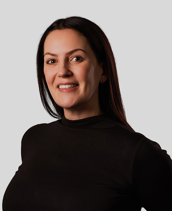Smiling woman with long dark hair wearing a black long-sleeve top against a plain gray background.