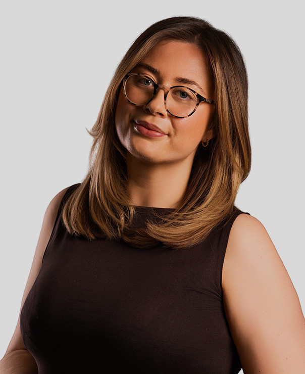 Woman with shoulder-length brown hair wearing tortoiseshell glasses and a sleeveless black top.