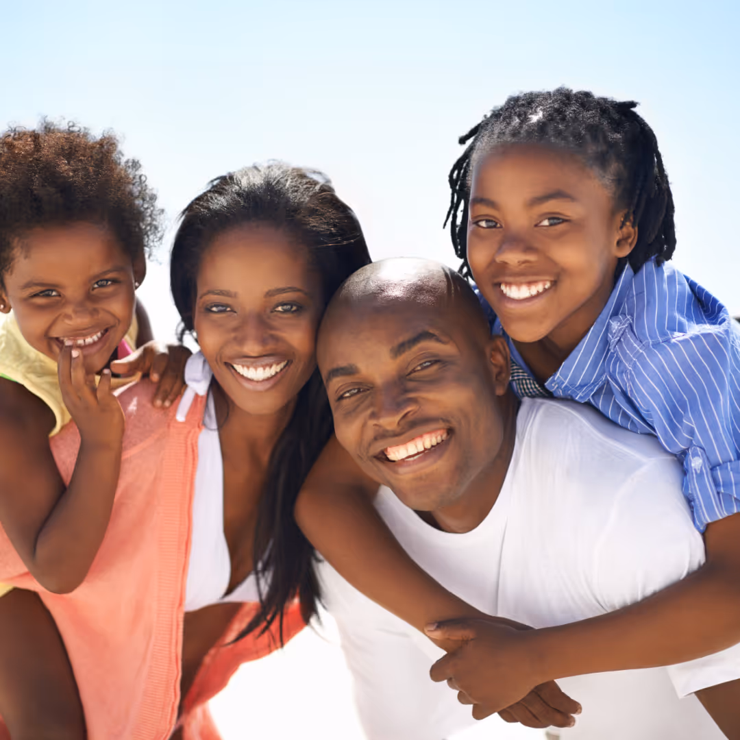 Smiling family of four embracing on a bright sunny day.