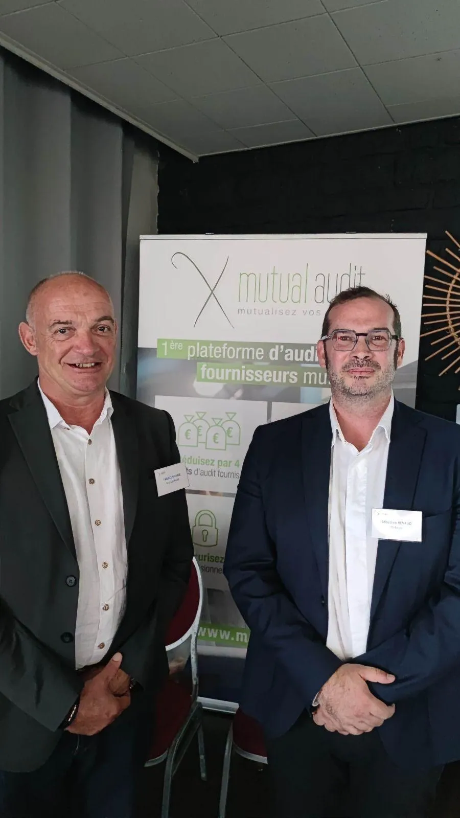 Deux hommes d'affaires souriants en costume debout devant une bannière de mutual audit.