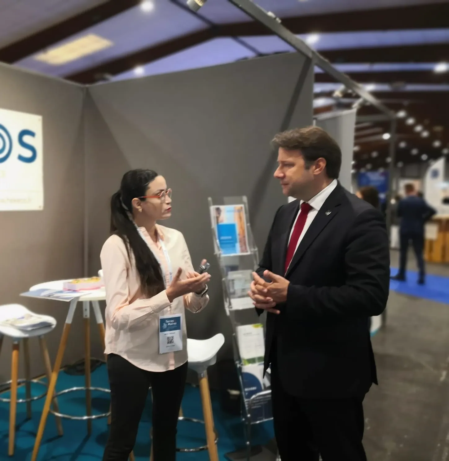 Deux professionnels en conversation au sein d'un stand d'exposition avec un présentoir de brochures à l'arrière.