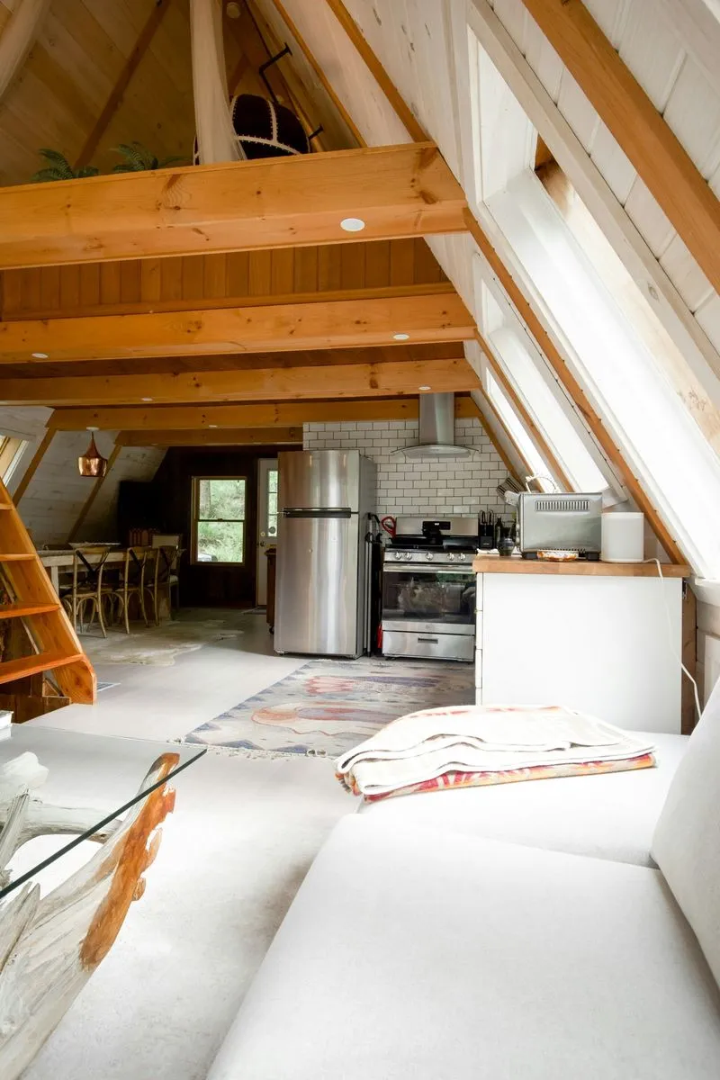 Spacious cabin interior with exposed wood beams, cozy seating, and a modern kitchen area featuring stainless steel appliances.