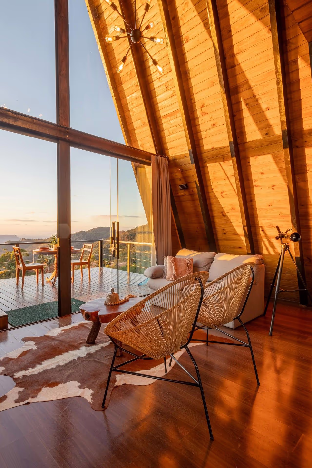 Cozy modern living room with wood accents, panoramic windows, and stylish furniture overlooking a scenic landscape at sunset.