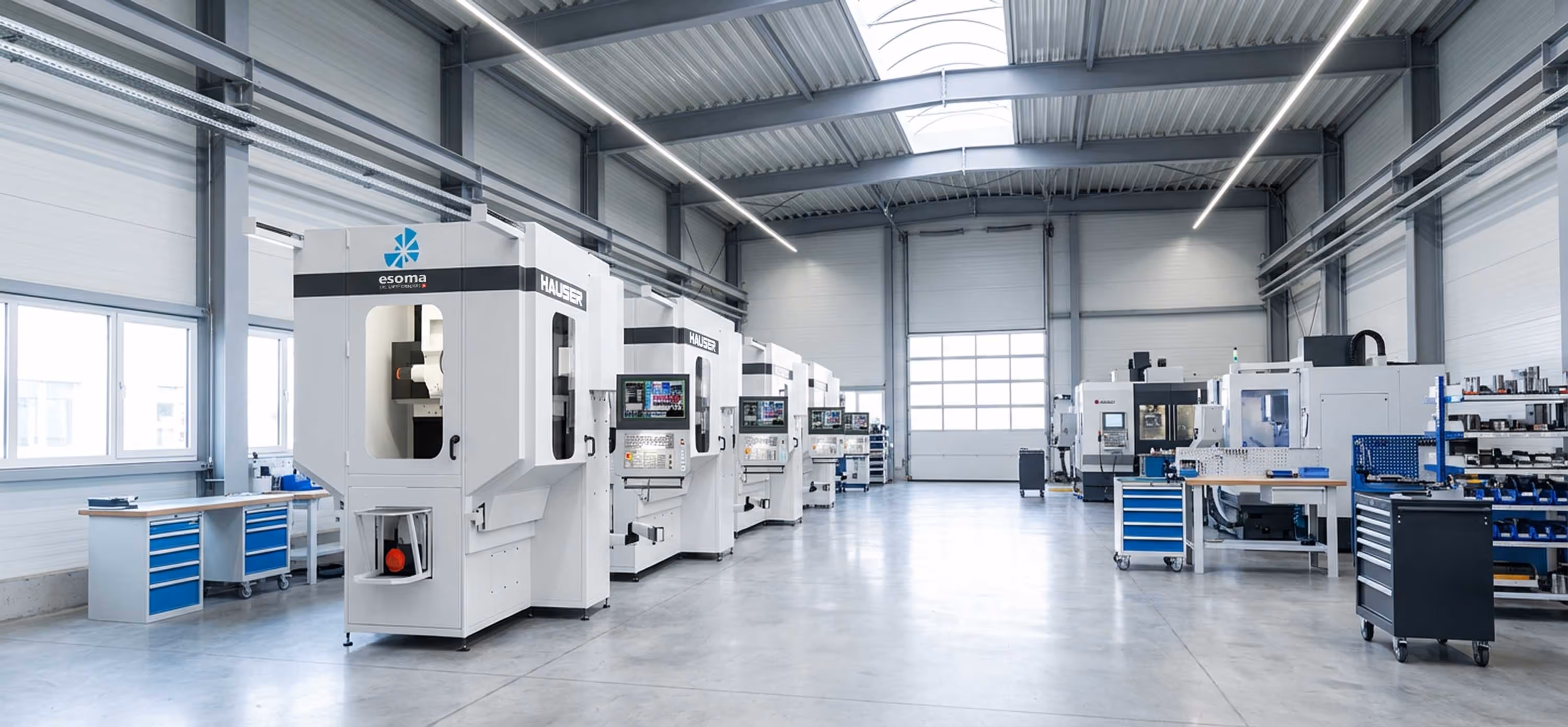 Moderne industrielle Werkstatt mit CNC-Maschinen und blauen Werkzeugwagen in heller Halle.