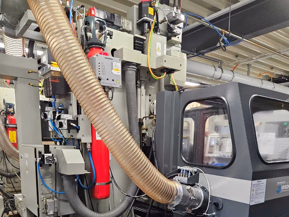 Industriemaschine mit großen Schläuchen, elektrischen Komponenten und rotem Feuerlöscher in Werkhalle.