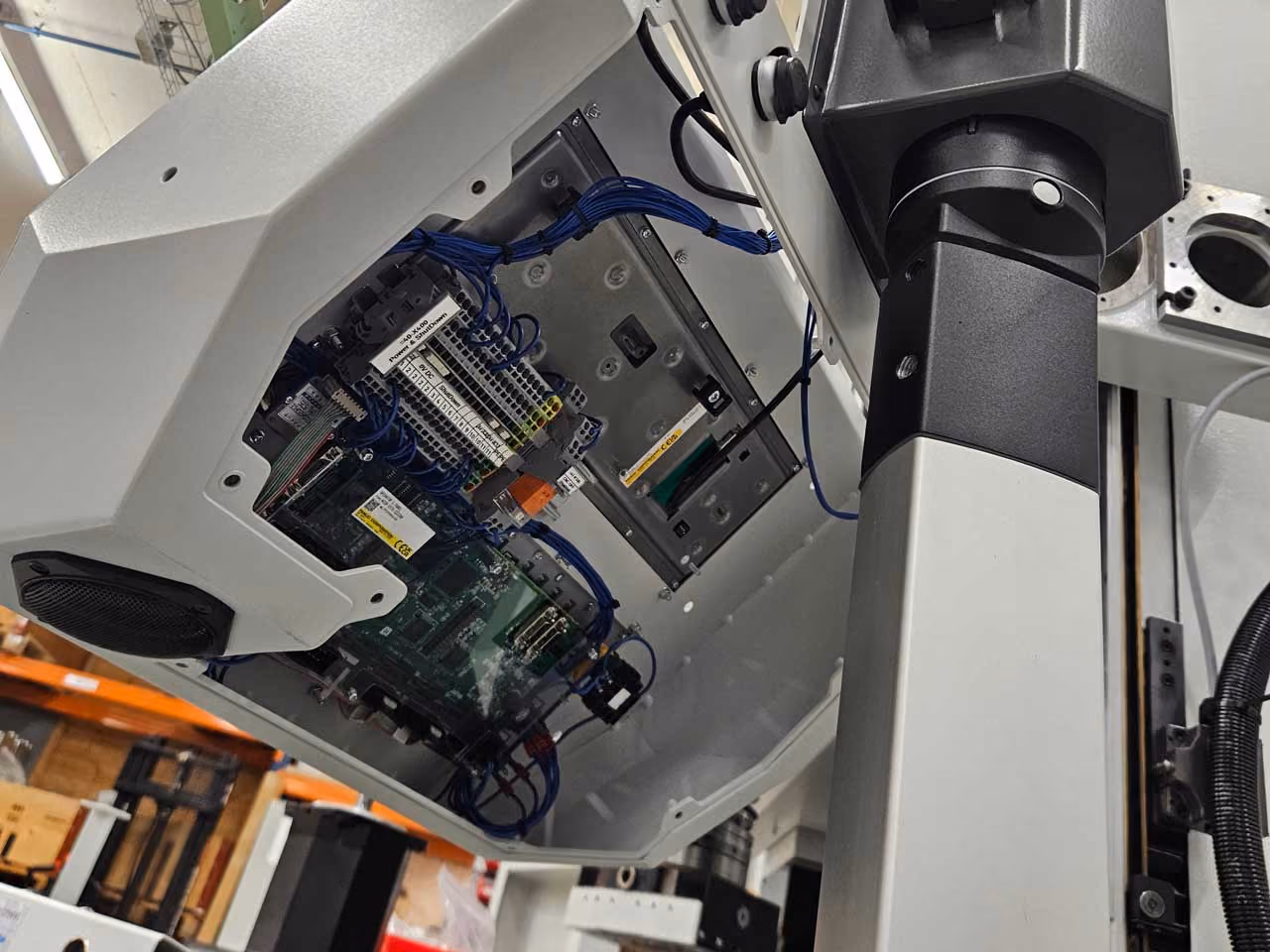Geöffneter Elektroschrank mit sichtbaren blauen Kabeln und elektronischen Komponenten in einer Werkstatt.