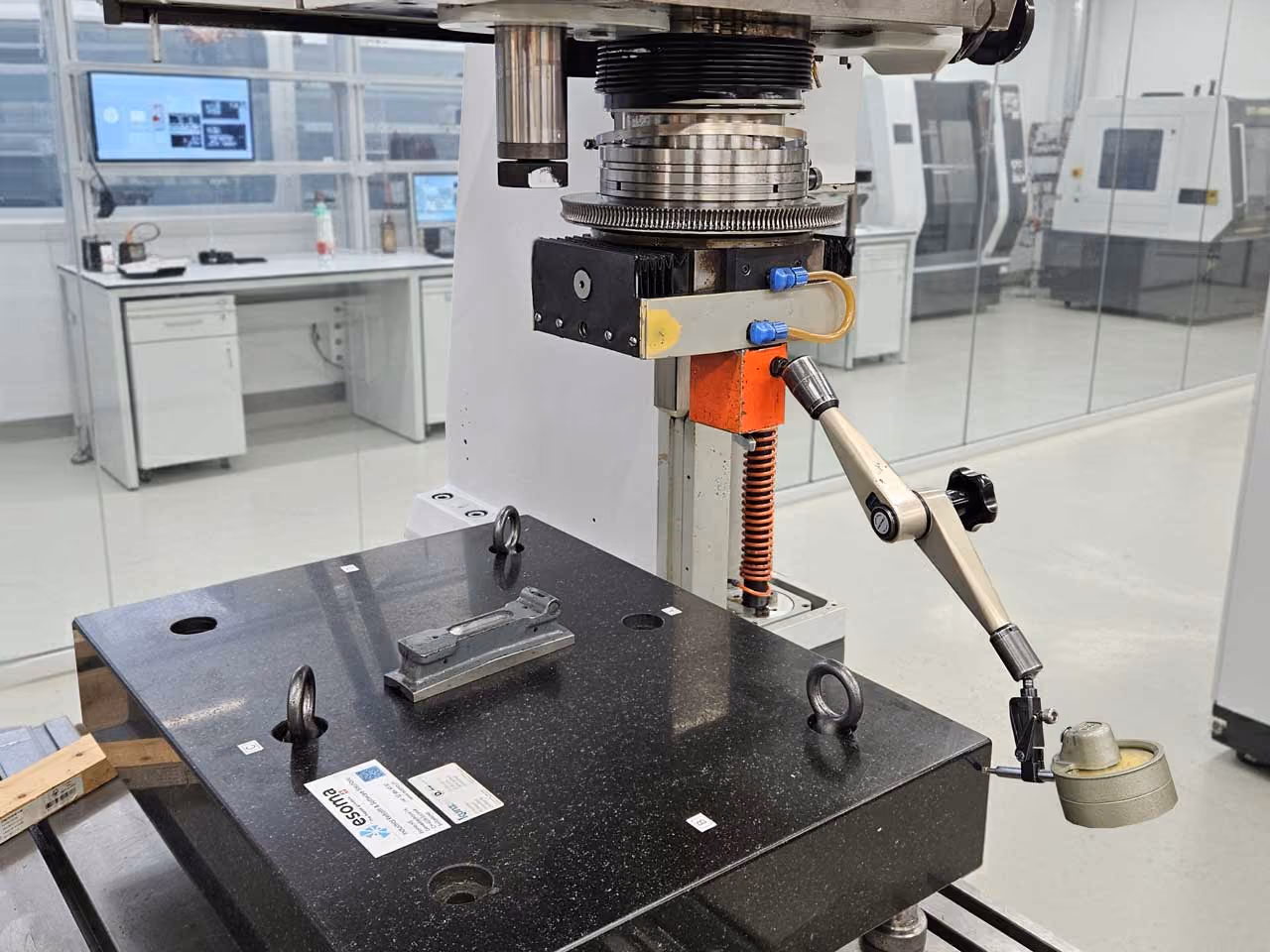 Messmaschine mit einem Halter und Abtastarm in einem modernen Labor mit Monitoren im Hintergrund.