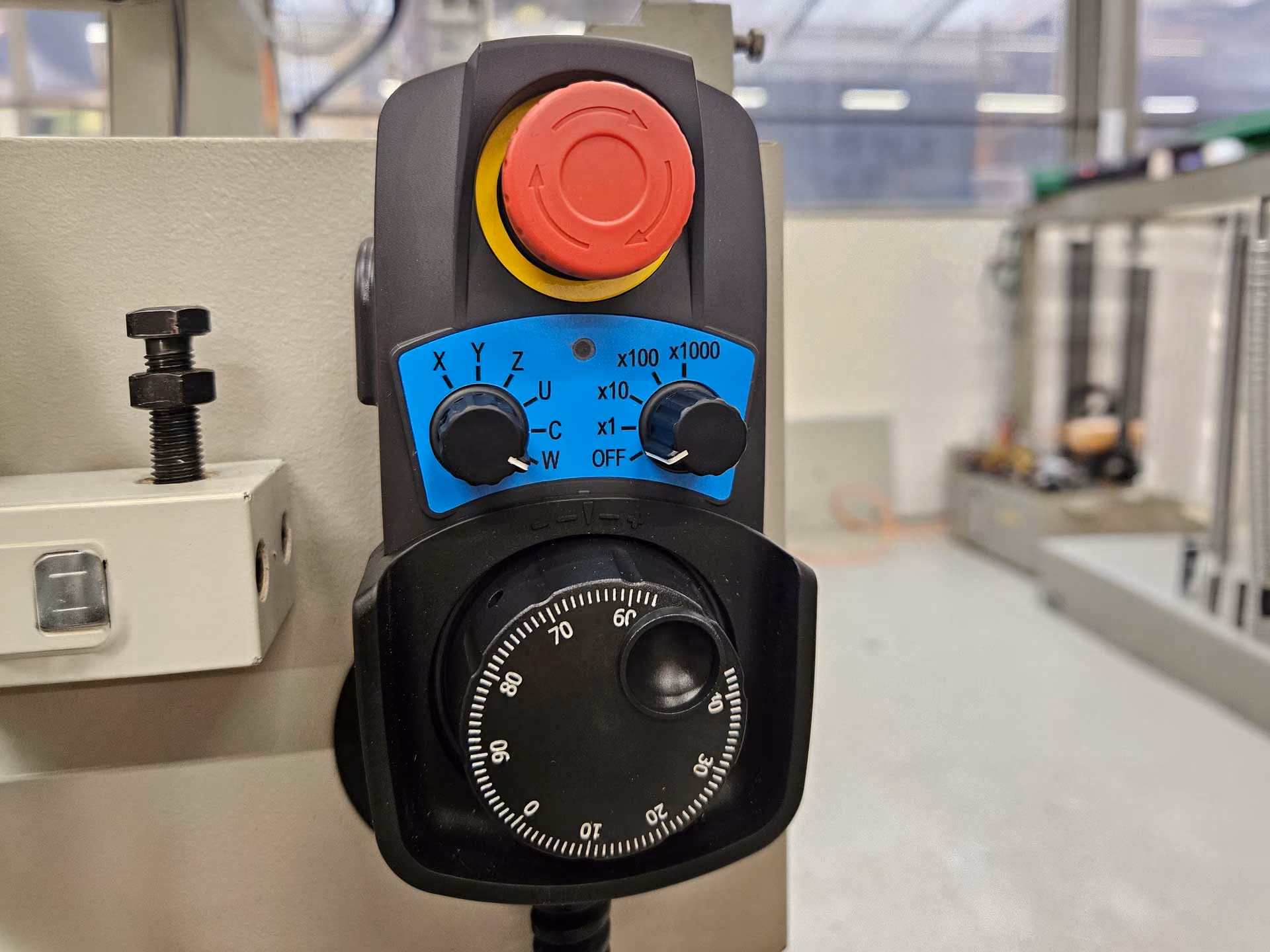 Handrad mit Skala, zwei Einstellrädern und rotem Not-Aus-Knopf an Maschinensteuerung.