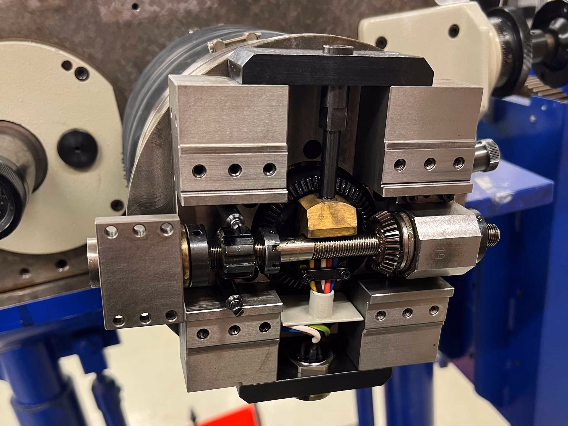 Nahaufnahme einer Maschine mit Metallteilen, Schrauben und Drähten vor unscharfem Hintergrund.