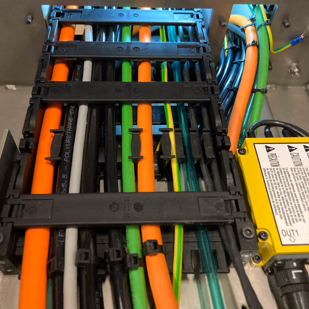 Bunte Kabel geordnet und befestigt in einem metallischen Technikgehäuse mit gelbem Warnaufkleber.