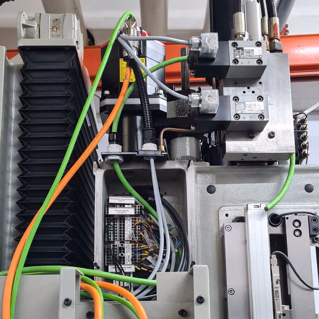 Nahaufnahme von elektrischem Steuergerät mit Kabeln und Hydraulikventilen an Industrieanlage.