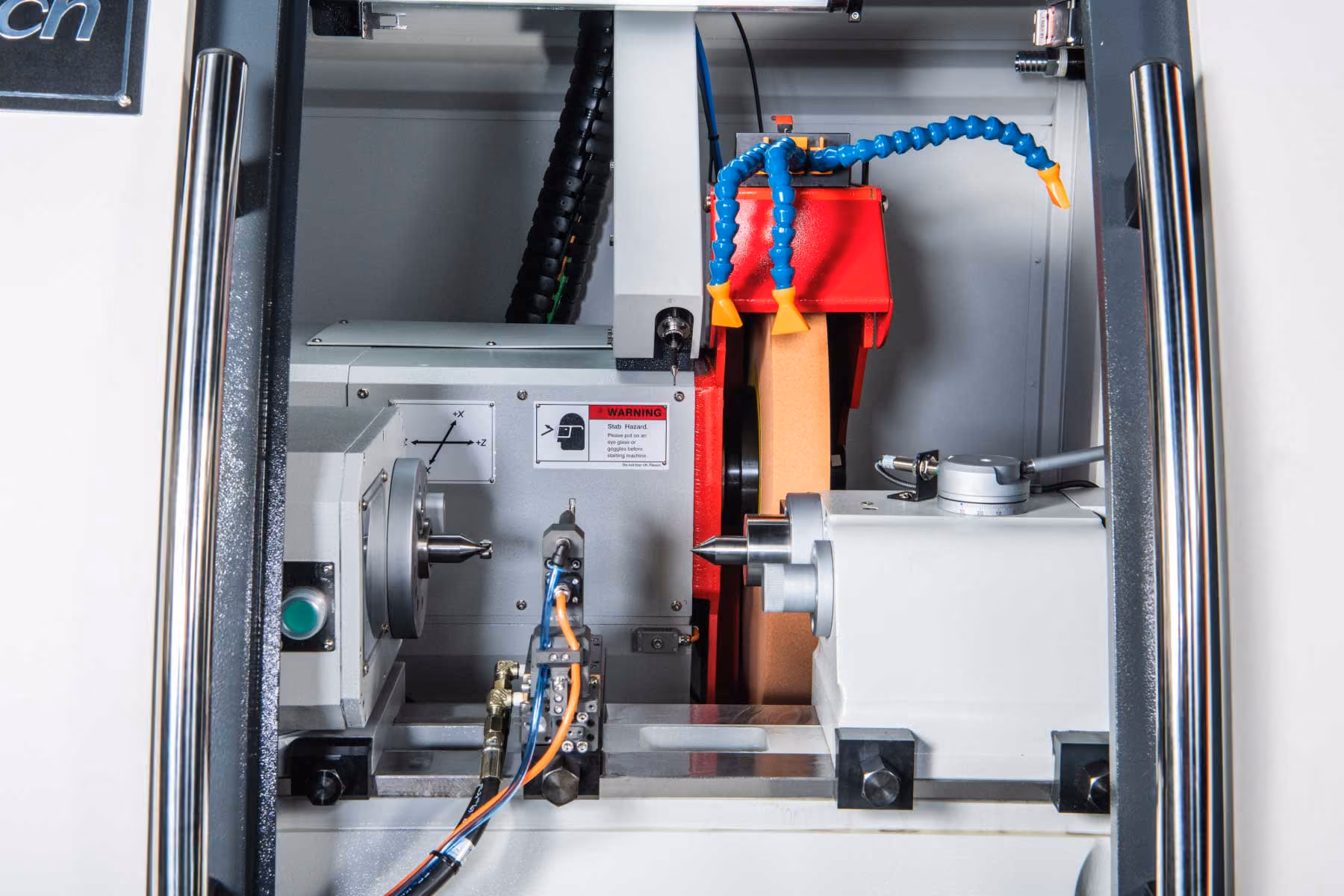 Innenansicht einer CNC-Maschine mit Spindeln, Kühlschläuchen und Sicherheitshinweis.