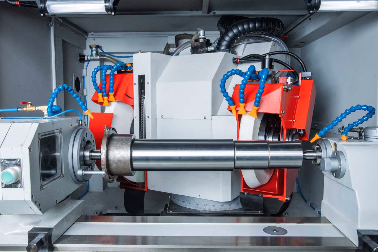 Industrielle Schleifmaschine mit einem zylindrischen Metallteil zwischen zwei Spannvorrichtungen.