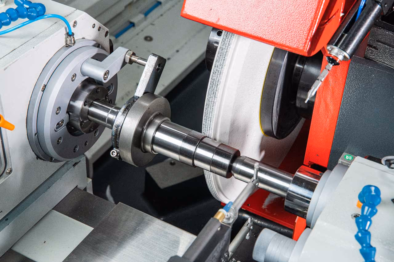 Industrielle CNC-Maschine schleift eine Metallwelle mit rot-weißer Schleifscheibe.
