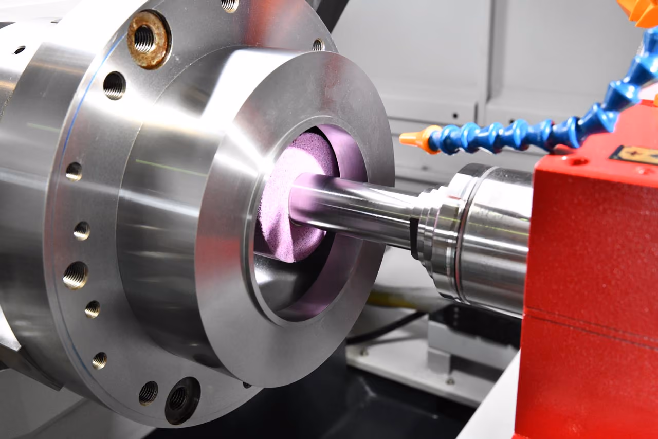 Präzisionsmaschine schleift eine Metallwelle mit einem rosa Schleifstein.
