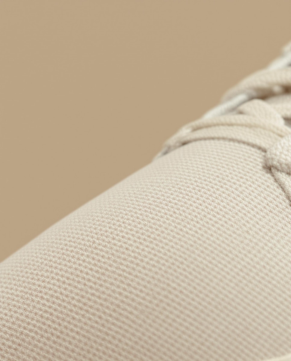 Close-up of beige textured fabric with visible laces, likely part of a shoe.