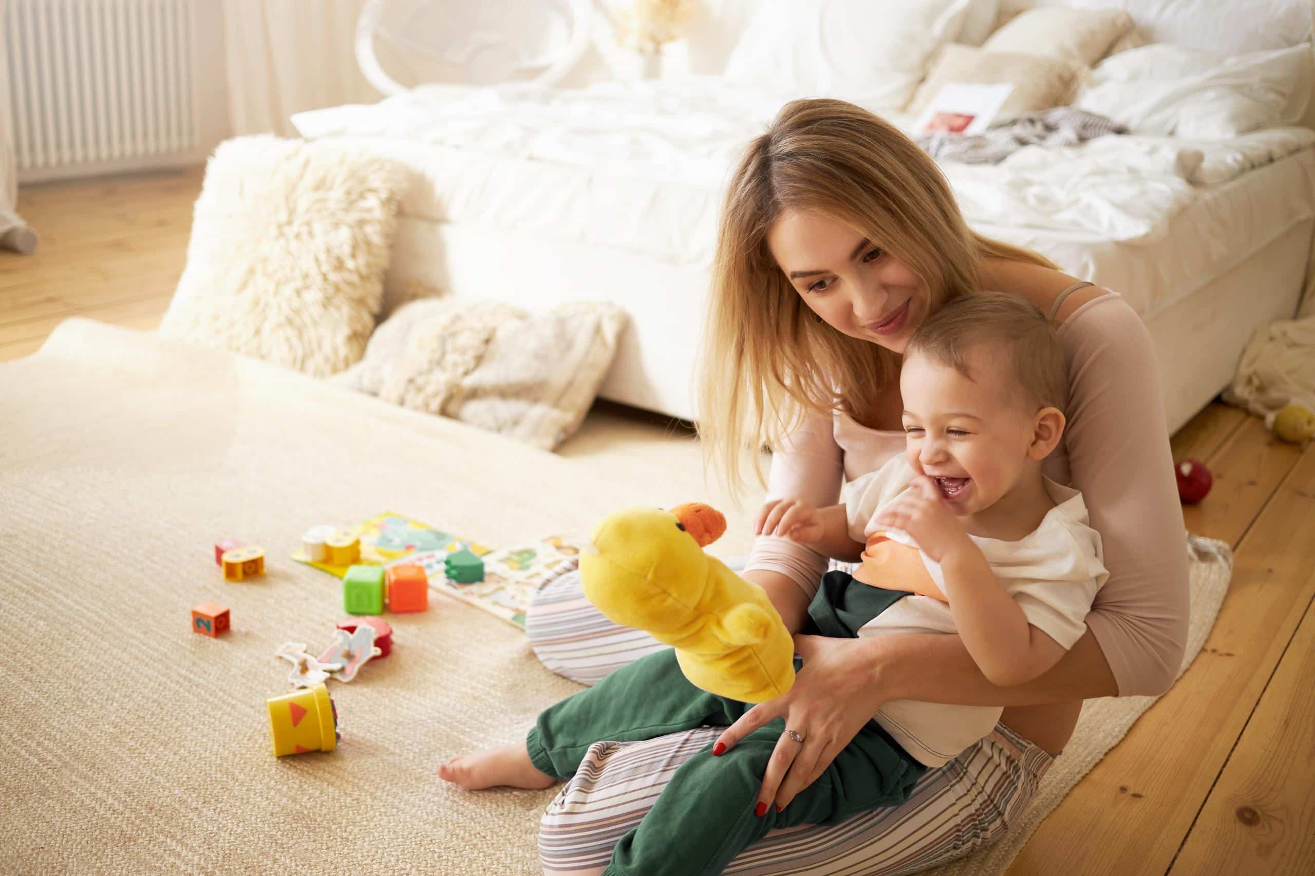 Nanny playing with a toddler and a stuffed duck toy on the floor at home
