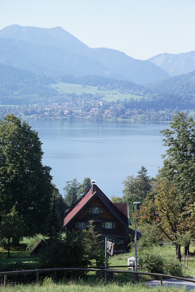 Foto von <a href="https://unsplash.com/de/@tkaiser?utm_source=unsplash&utm_medium=referral&utm_content=creditCopyText">t Kaiser</a> auf <a href="https://unsplash.com/de/fotos/ein-haus-auf-einem-hugel-mit-einem-see-im-hintergrund-gcUF3wiiZbg?utm_source=unsplash&utm_medium=referral&utm_content=creditCopyText">Unsplash</a>
